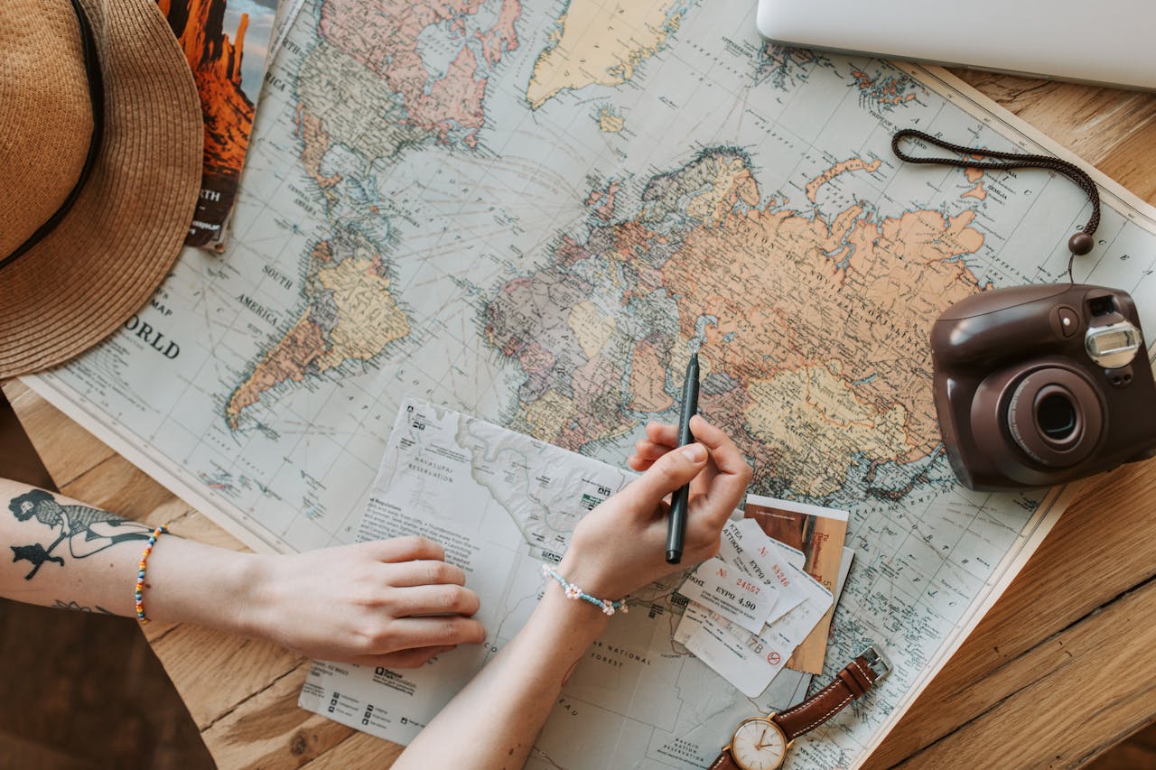 Top view of a womans hands planning a trip with a map, camera, and travel items.